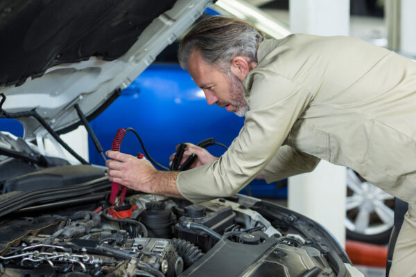 Mechanic attaching jumper cables to car battery in repair garage