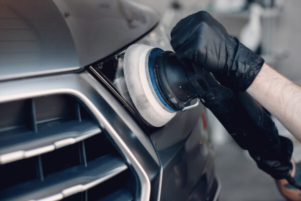 Man in a garage. Worker polish a car.